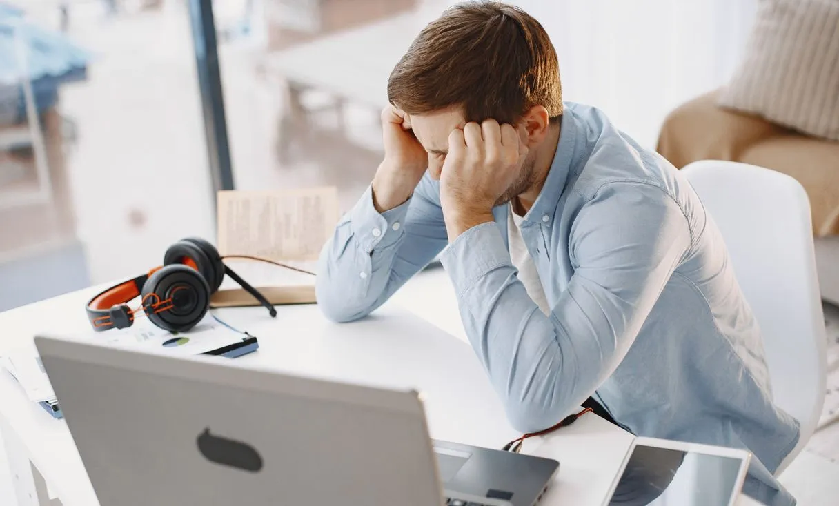 Homem em escritório parece frustrado enquanto trabalha no notebook, representando: Internet caindo ou lenta na empresa? Veja o que fazer