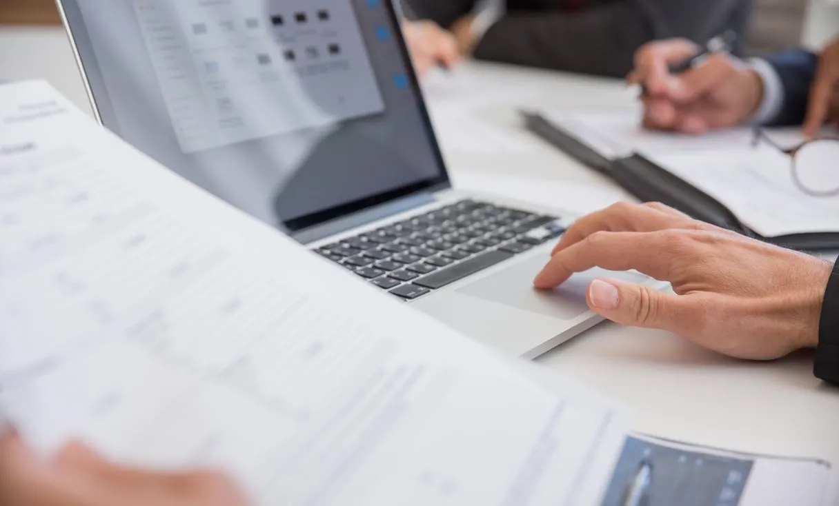 Mãos trabalhando em documentos e notebook em mesa de escritório representando: Arquivos da Área de Trabalho somem? Como parar isso redirecionando para o OneDrive