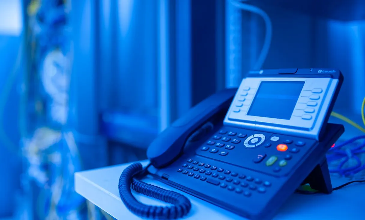 Close de um telefone IP de escritório com luz azul representando: Ramal IP caindo? Como evitar parar a telefonia