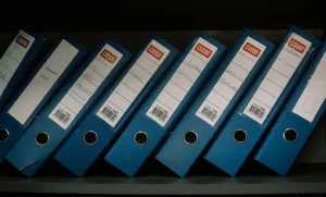 Pasta com fichários organizados em prateleira representando: Sem inventário de TI? Como parar de perder equipamento