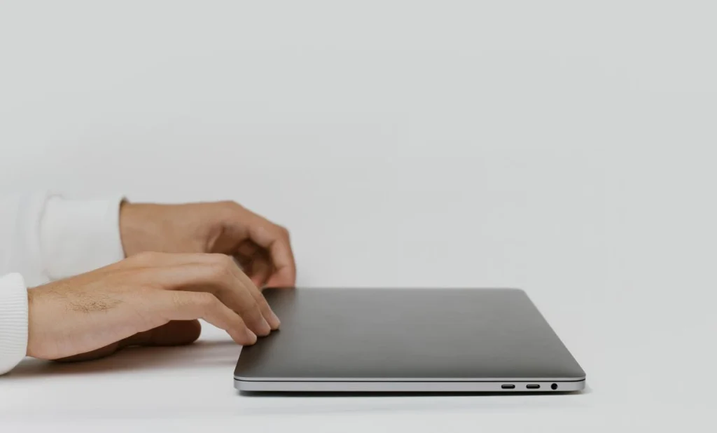 Mãos abrindo um notebook sobre a mesa representando: Novo colaborador? E-mail, Teams e pastas prontos no dia 1